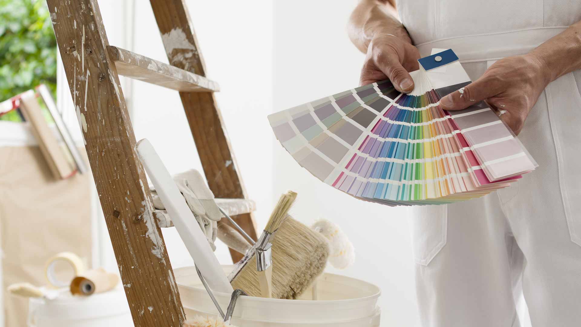 Painting standing with ladder and tools, holding out a book of paint swatches