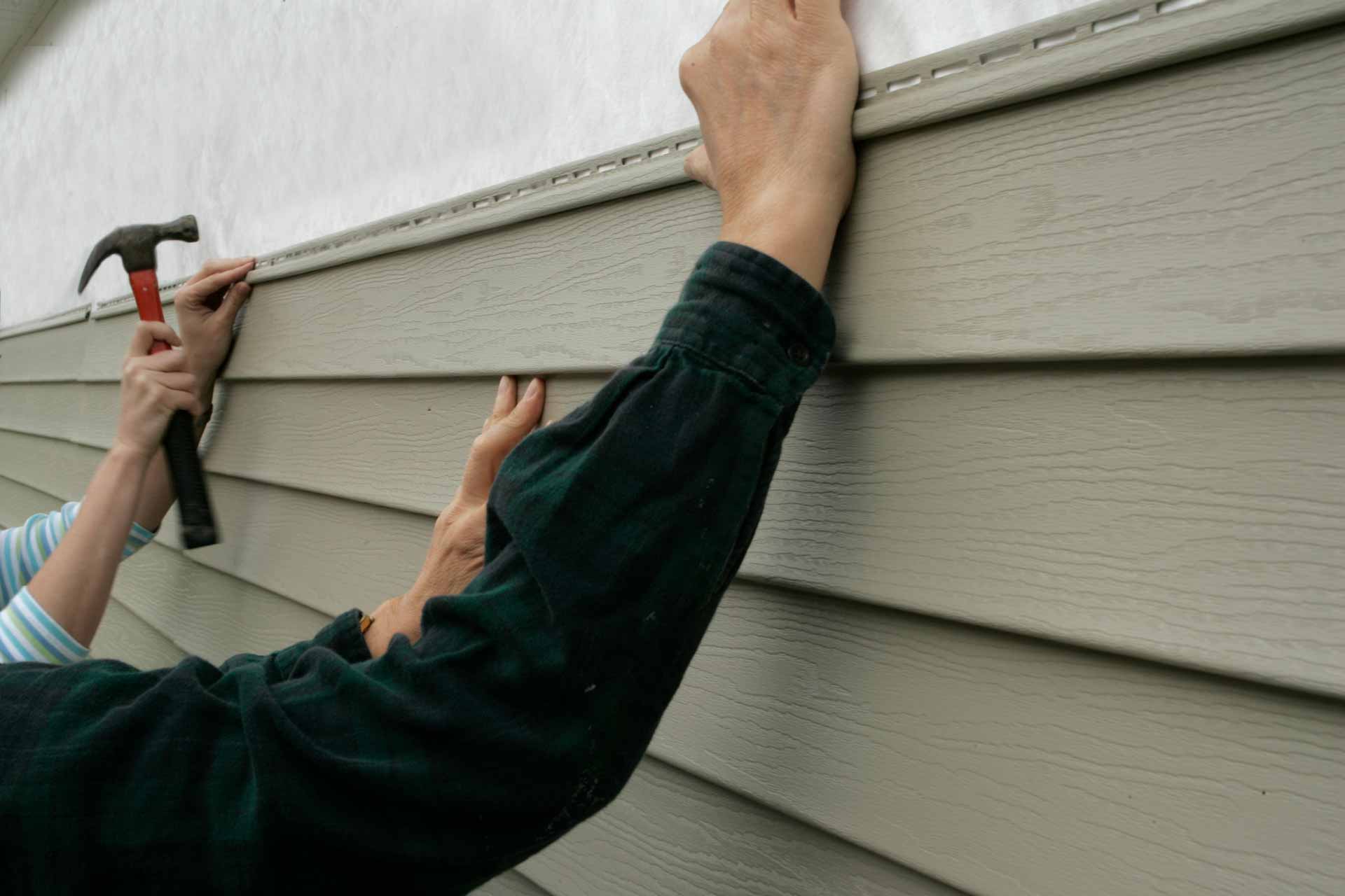 Two people installing vinyl siding on a house