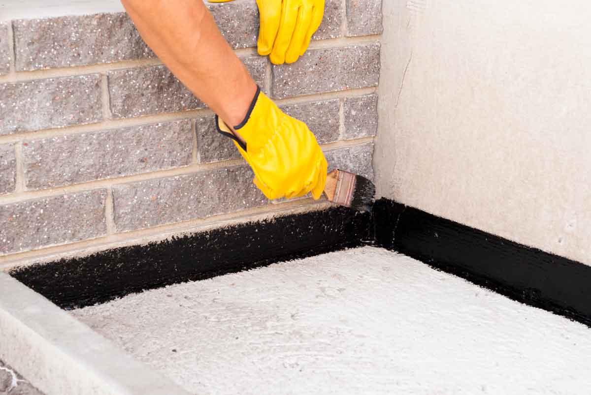 Basement waterproofing contractor applying bitumen waterproof membrane to basement walls